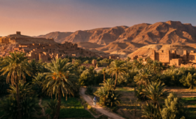 Rural Morocco countryside with palm oasis, traditional kasbah, and Atlas Mountains at sunset