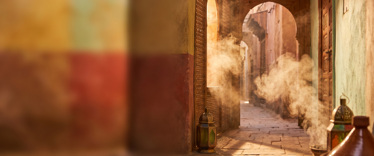 Golden sunset light streaming through a traditional Marrakech archway with warm spice-toned hues and soft drifting steam, evoking the sensory atmosphere of a Moroccan food tour.