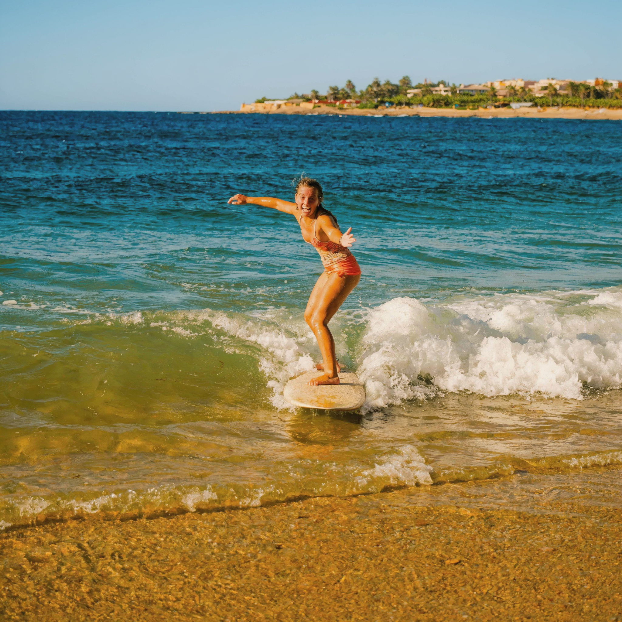 Beginner surfer riding a gentle wave at Aourir Banana Village Taghazout Morocco beach, soft rolling wave, golden sand, warm sunlight