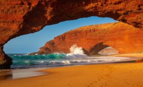 Discover the most beautiful beaches in Morocco: golden sunset at Legzira Beach with iconic red rock arches and turquoise Atlantic Ocean waves crashing on the shore