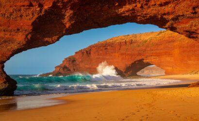 Discover the most beautiful beaches in Morocco: golden sunset at Legzira Beach with iconic red rock arches and turquoise Atlantic Ocean waves crashing on the shore