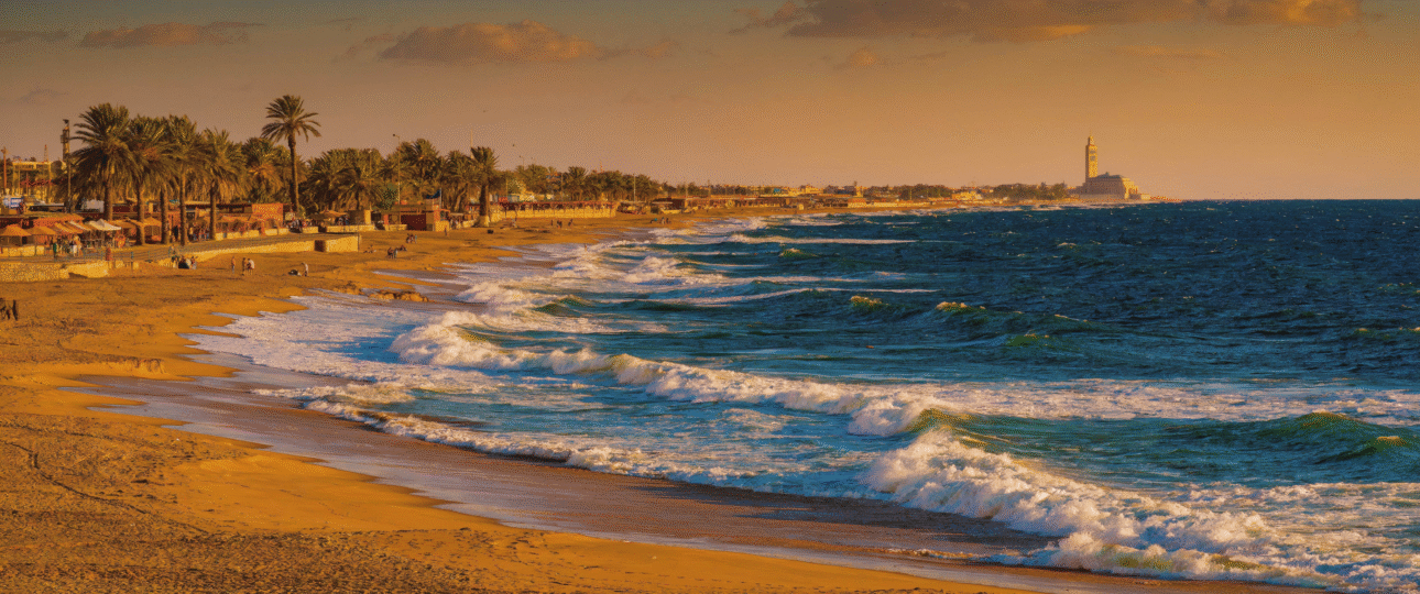 Panoramic view of Ain Diab urban beach along Casablanca Morocco coastline at golden hour, with Atlantic waves and city skyline, showcasing the best Casablanca Morocco beach experience