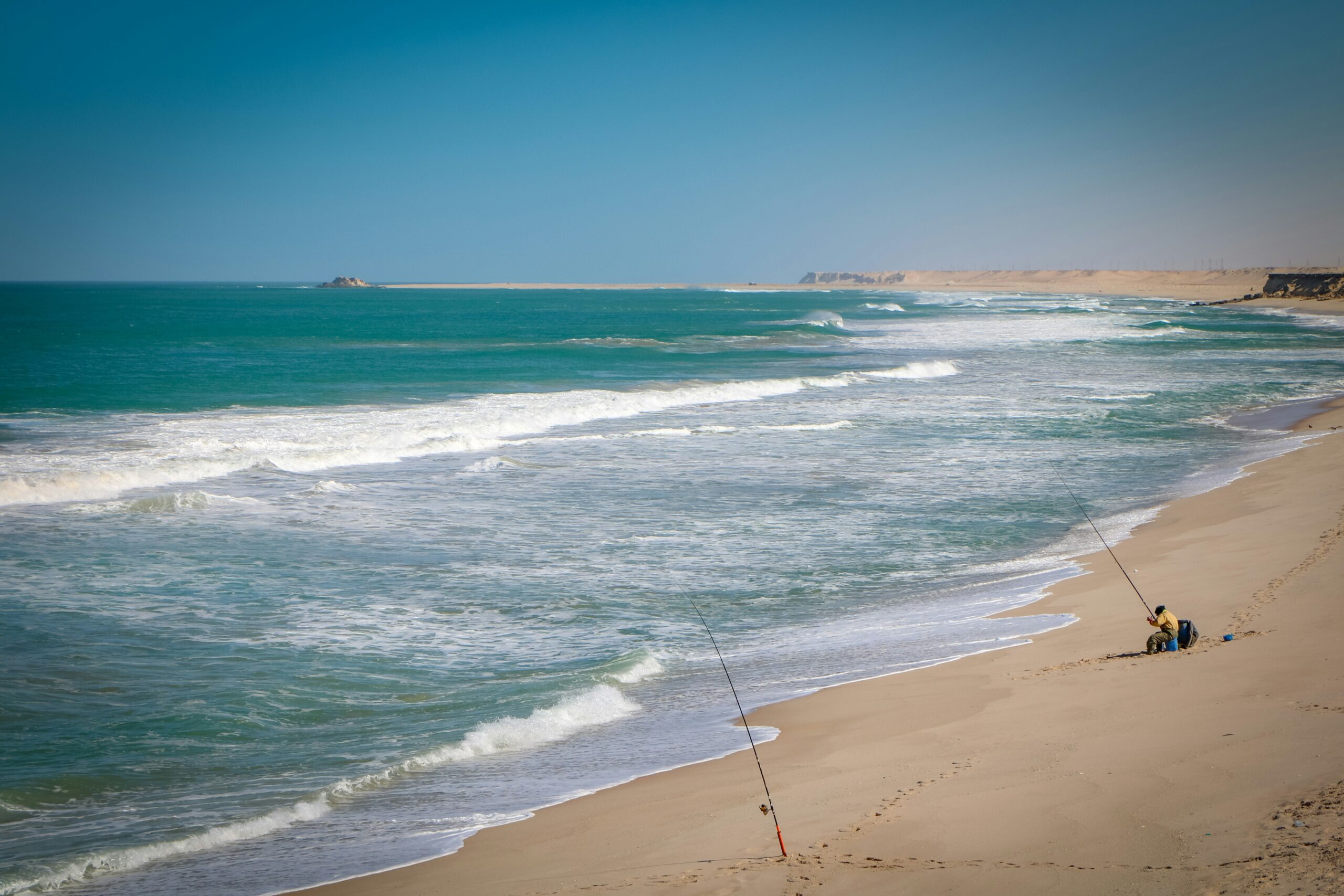 A beach scene with a lone fishing pole sticking out of the sand, Dakhla