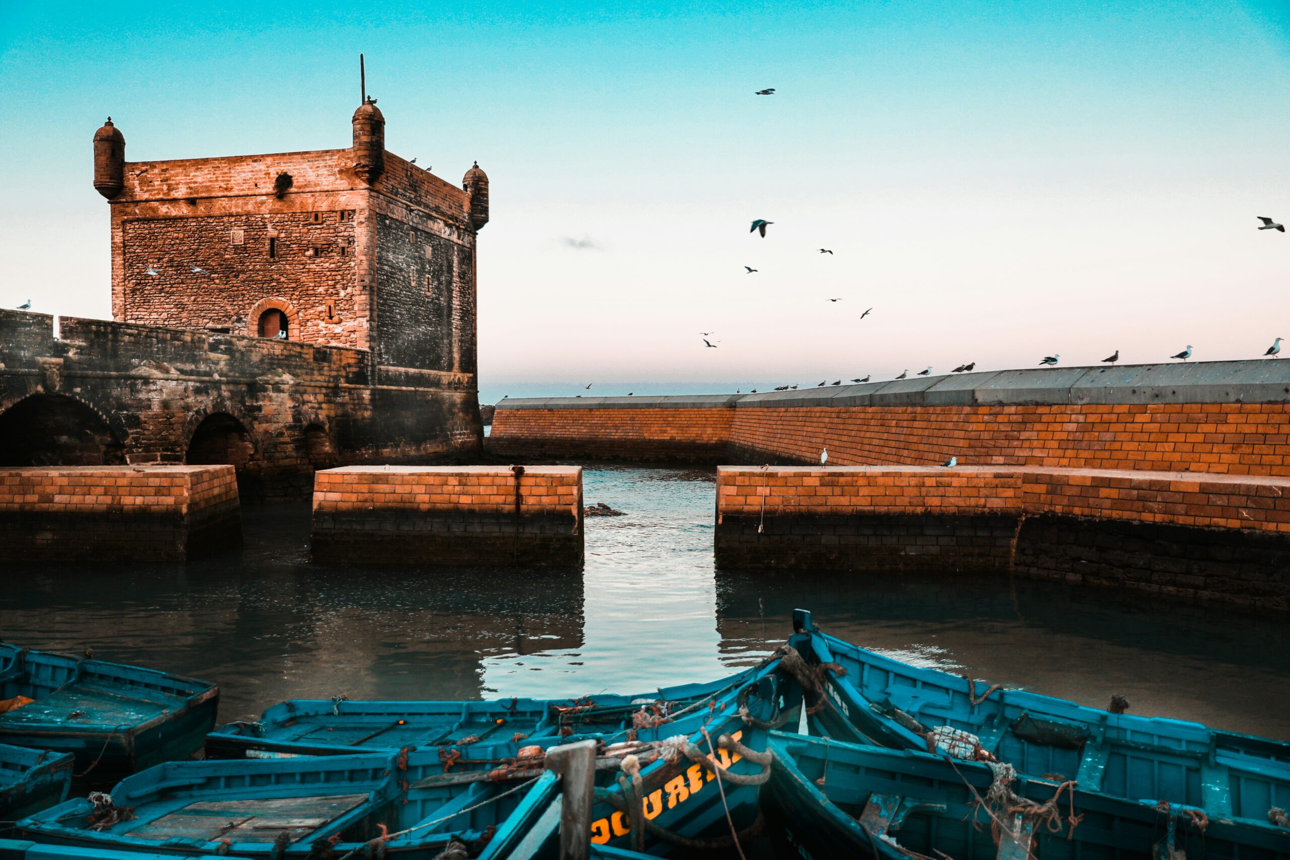 A large stone building with a tall tower, situated next to a body of water, Essaouira