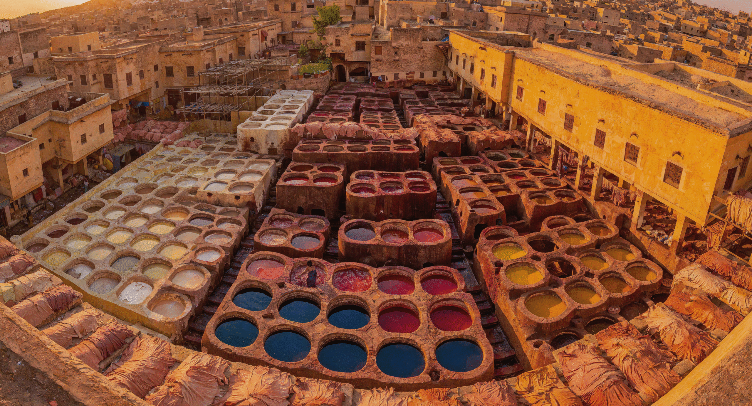Stunning aerial view of Chouara Tannery in the Fes Medina, Morocco, showing colorful natural dye pits and leather craftsmen at work during golden hour - essential guide to authentic leather goods Fes medina shopping.