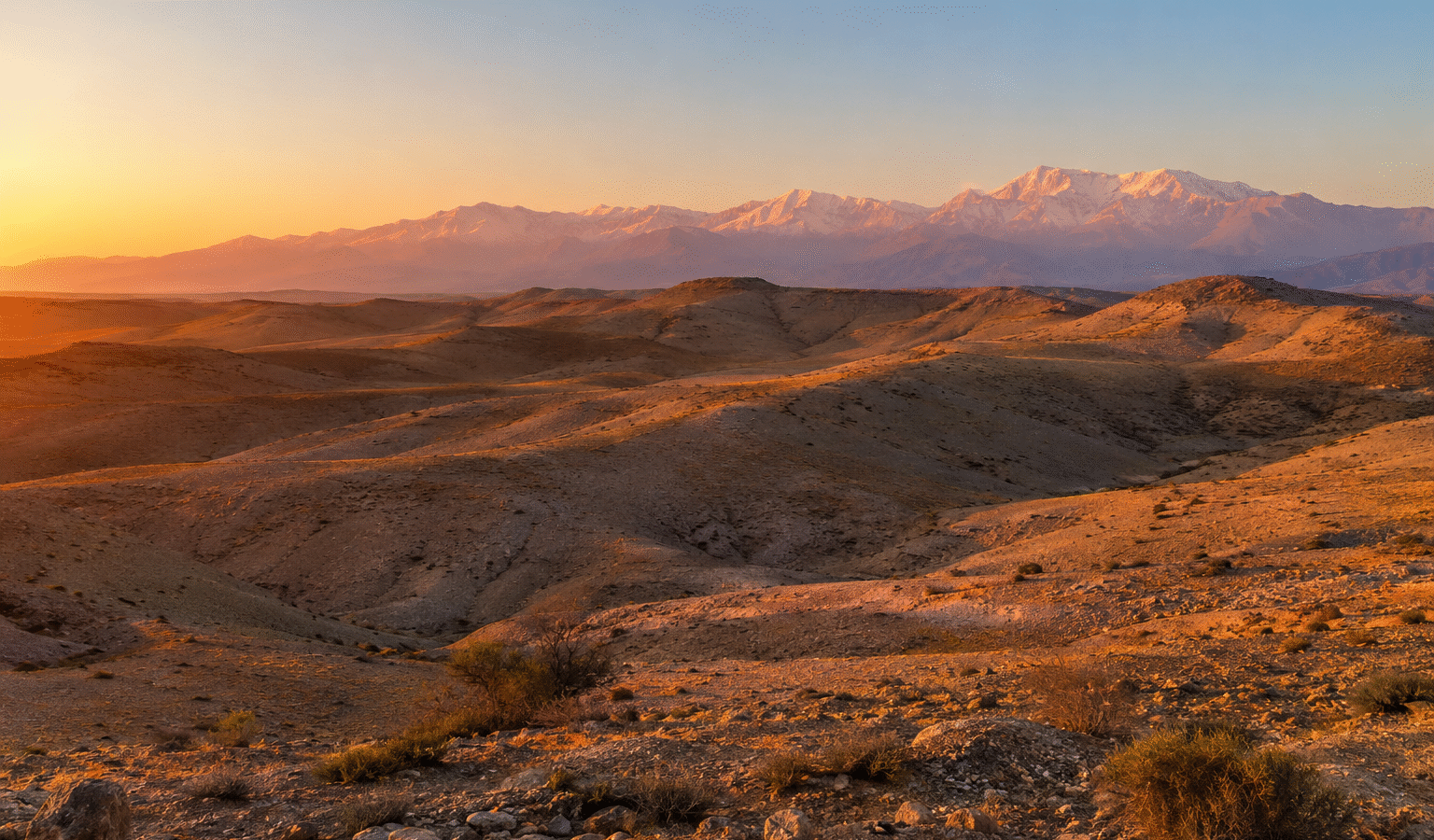 A desert landscape with several tents set up in the area. The tents are made of canvas and have wooden, Agafay desert camp